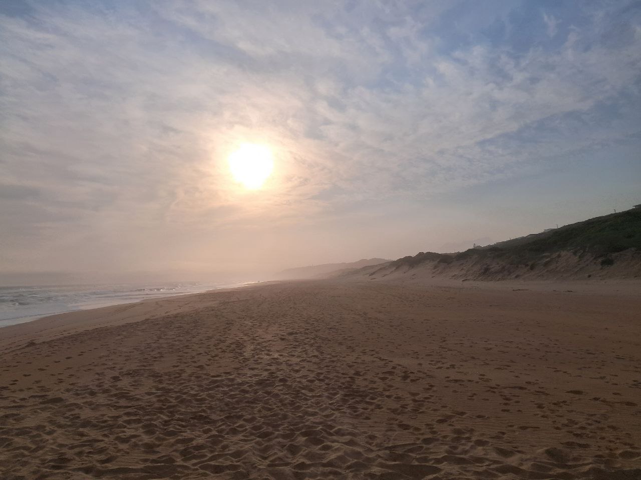 Sun setting over Wilderness Beach with dunes on the right and waves coming in